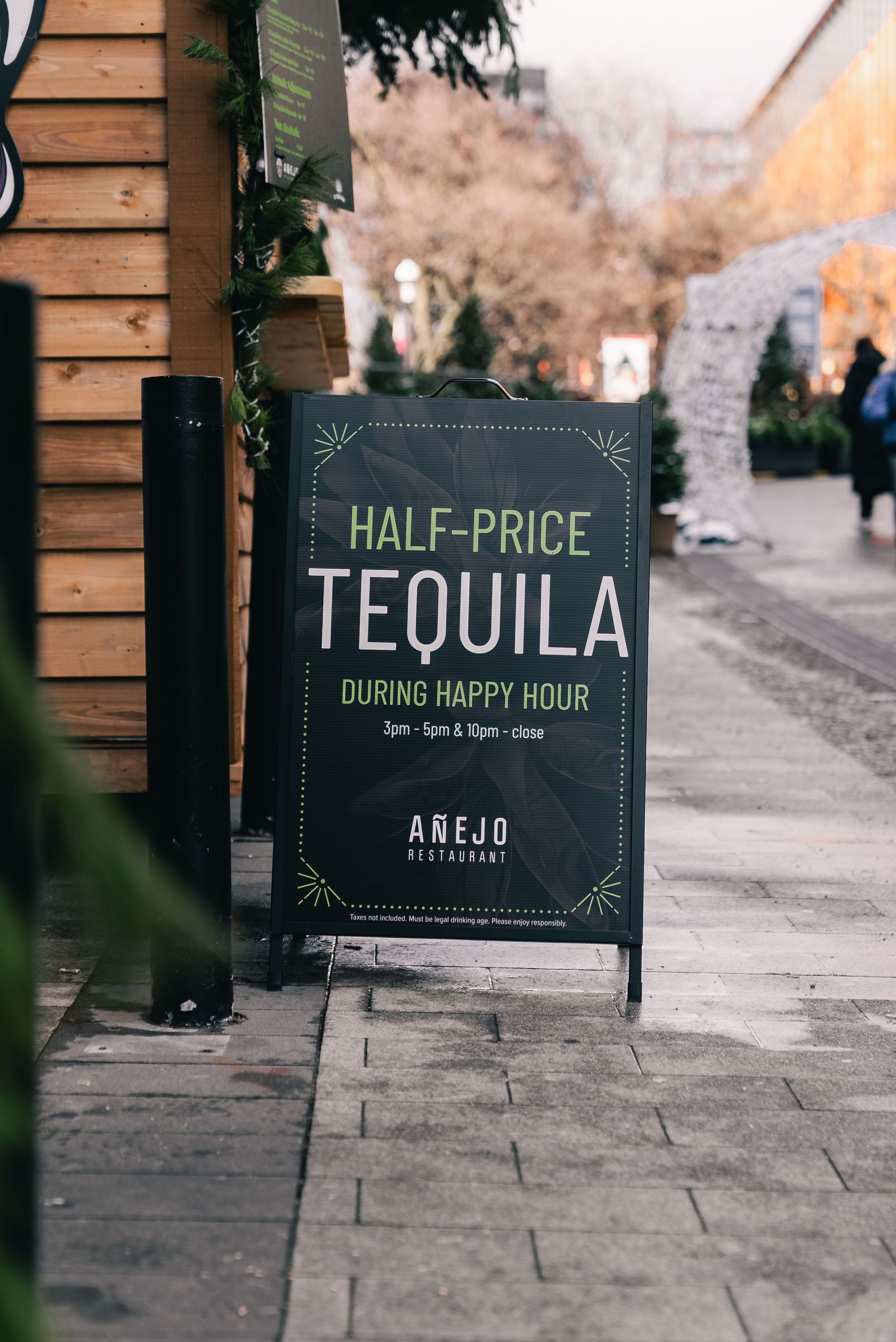 Sidewalk sign advertising half-price tequila at a bar, on a city street.