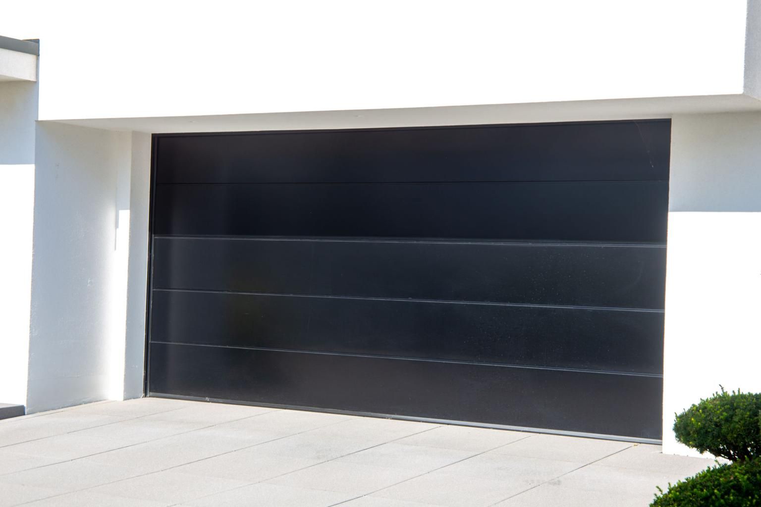 Modern white house with a large black garage door and driveway