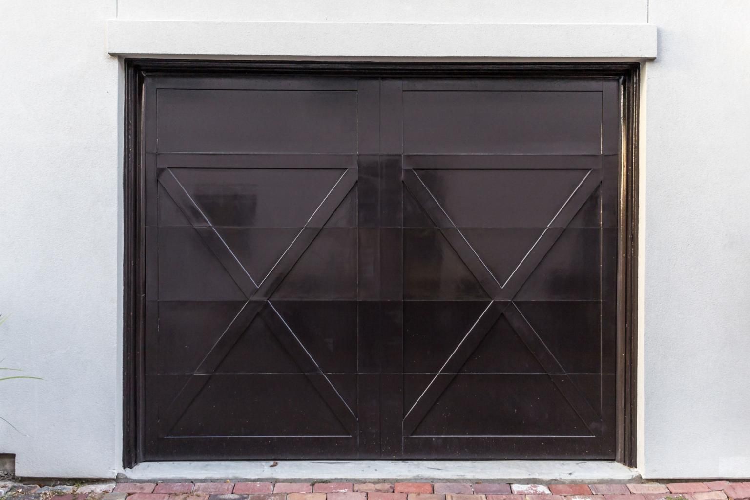 Dark metal garage door with diagonal X-bracing set in a white wall