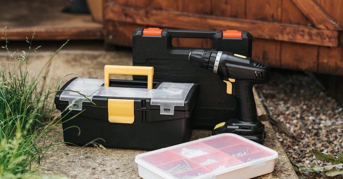 A drill and a toolbox are sitting on the ground next to a wooden shed.