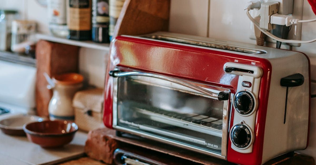 A red toaster oven is sitting on top of a wooden shelf in a kitchen.