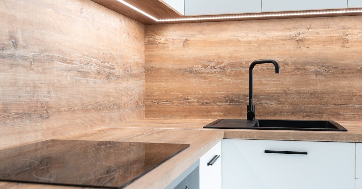 A kitchen with a stove top oven , sink , and wooden wall.