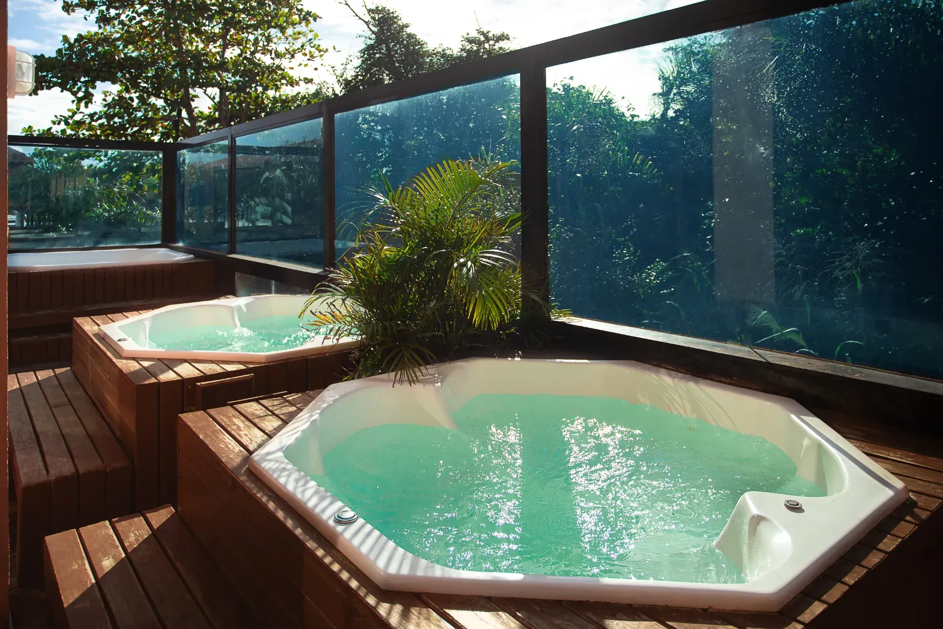 Terraço no quintal com duas banheiras de hidromassagem octogonais e um guarda-corpo de vidro com vista para as árvores e a água.