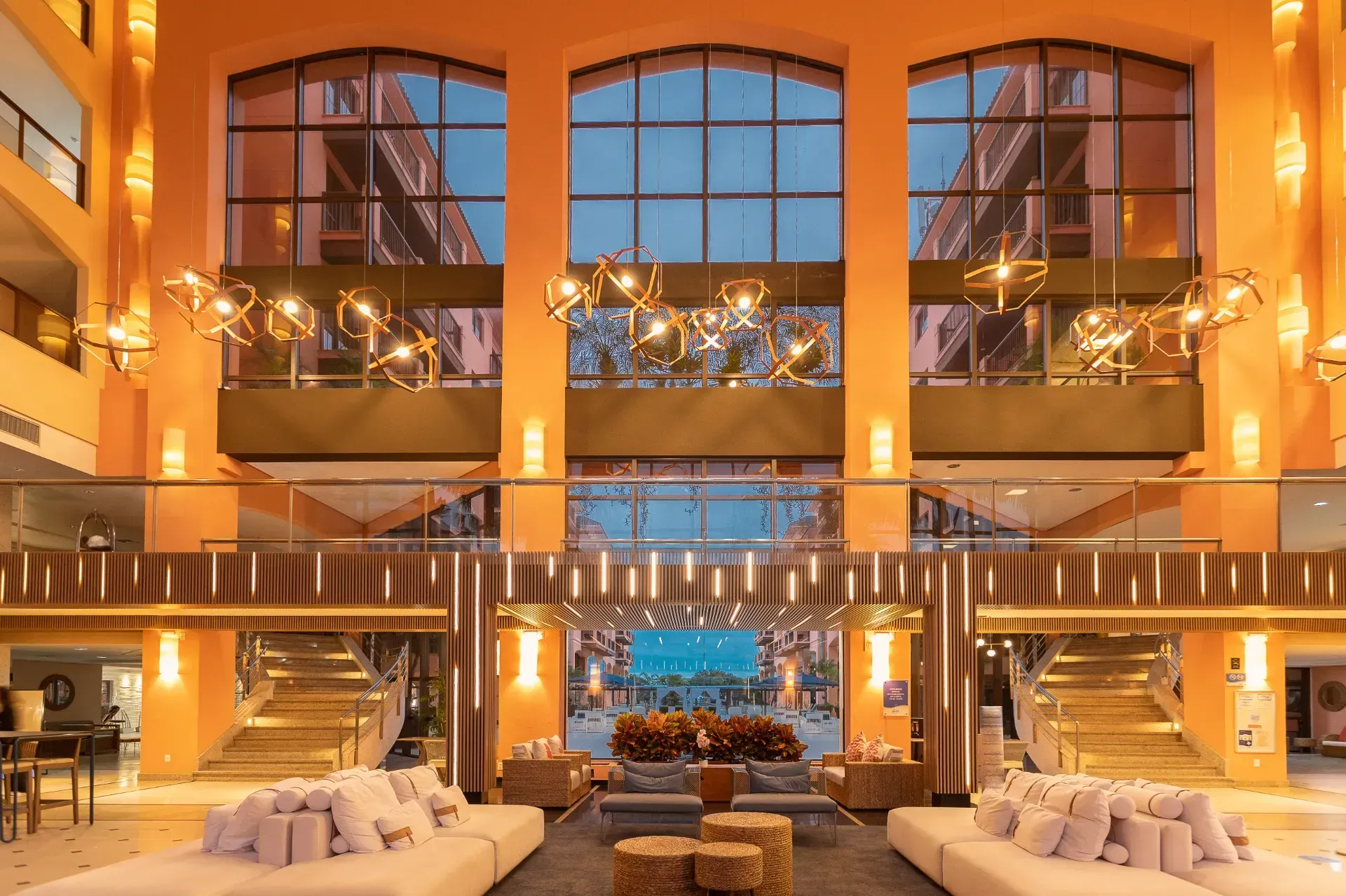 Lobby de hotel de luxo com iluminação aconchegante, janelas altas, lustres e sofás brancos voltados para uma área de estar central.