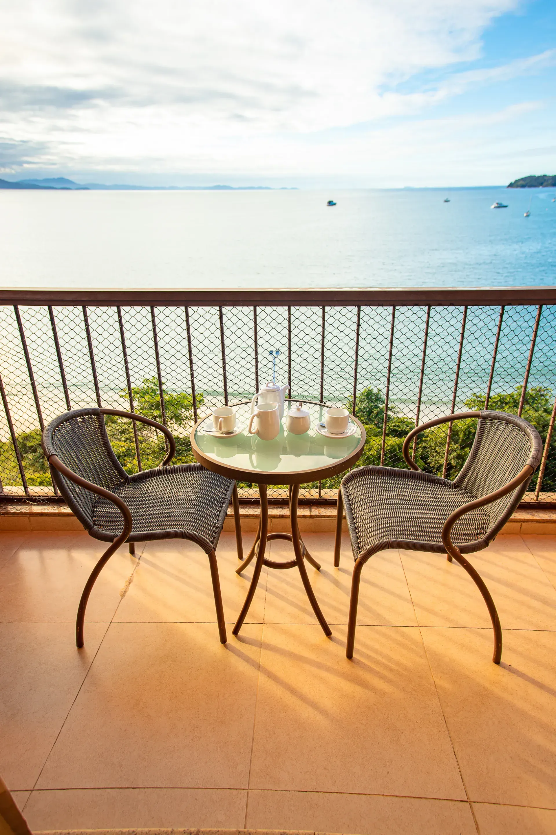 Mesa de pátio com duas cadeiras de vime com vista para o oceano calmo ao pôr do sol.