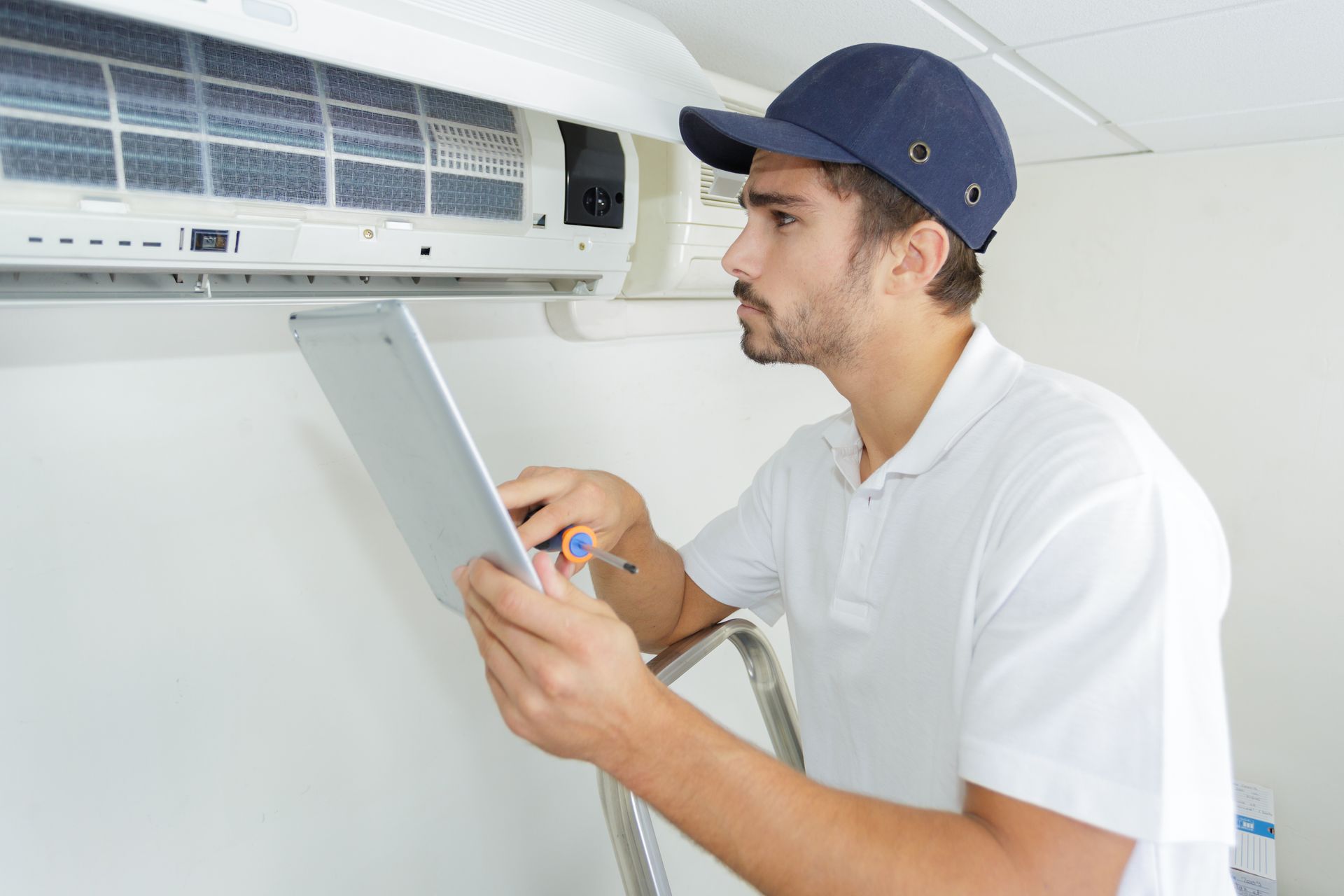 A man is looking at a tablet while working on an air conditioner.
