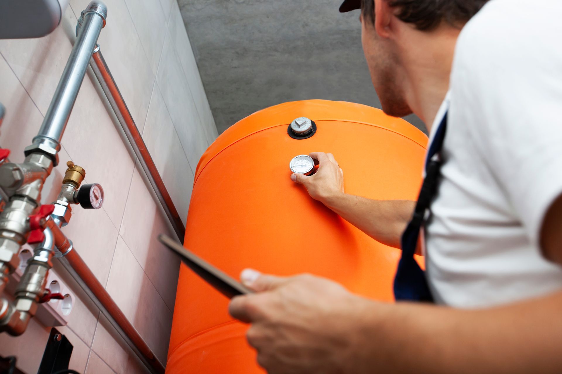 A man is working on an orange tank while holding a tablet