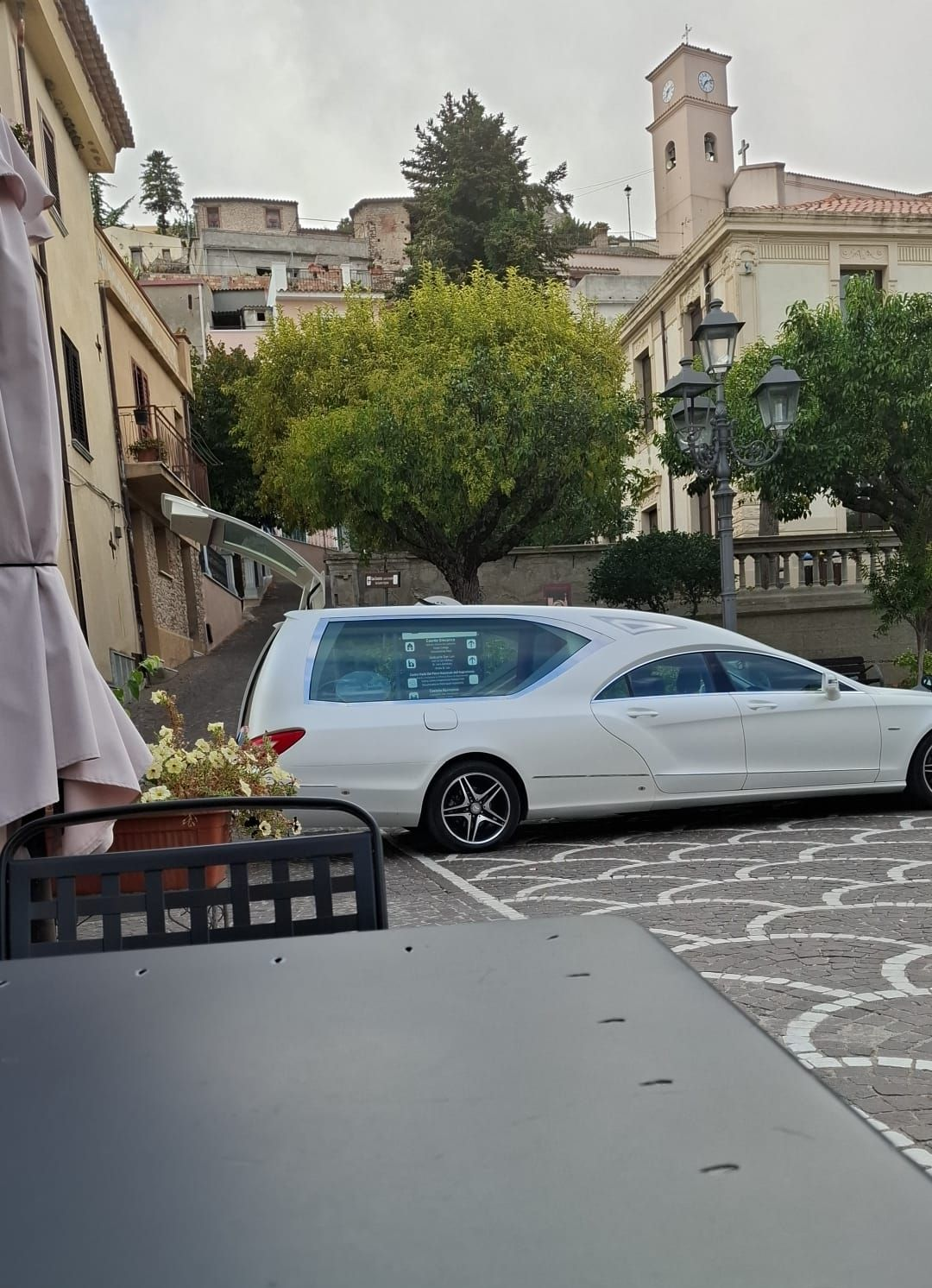 Donna sorridente con maglietta rosa e occhiali, con un addetto alle pulizie sullo sfondo che spolvera uno scaffale.