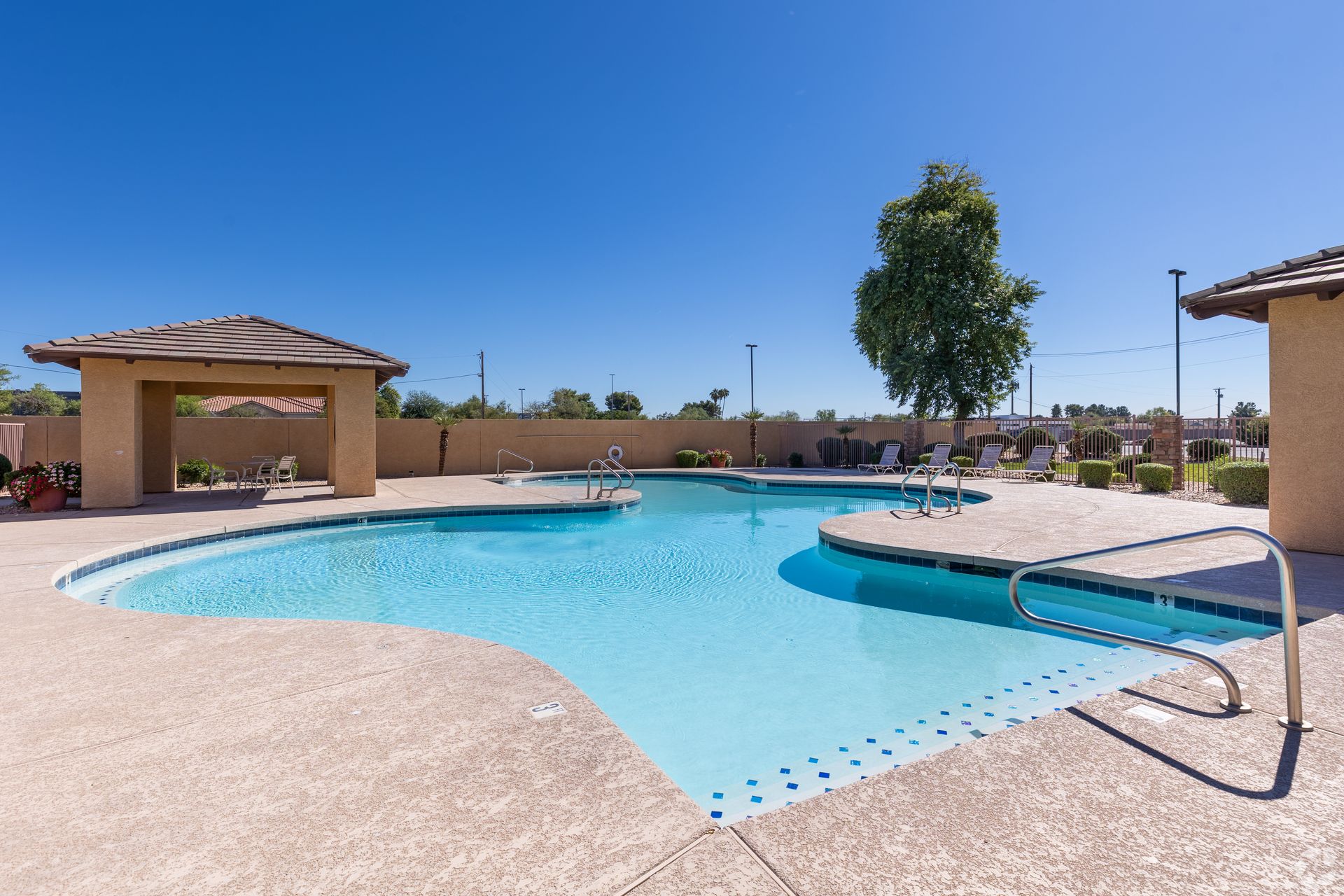 A swimming pool with a blue surface, stone patio, and a covered pavilion under a clear blue sky.