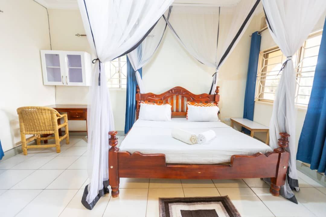 Bright bedroom with wooden bed, white canopy curtains, wicker chair, and blue drapes by the windows