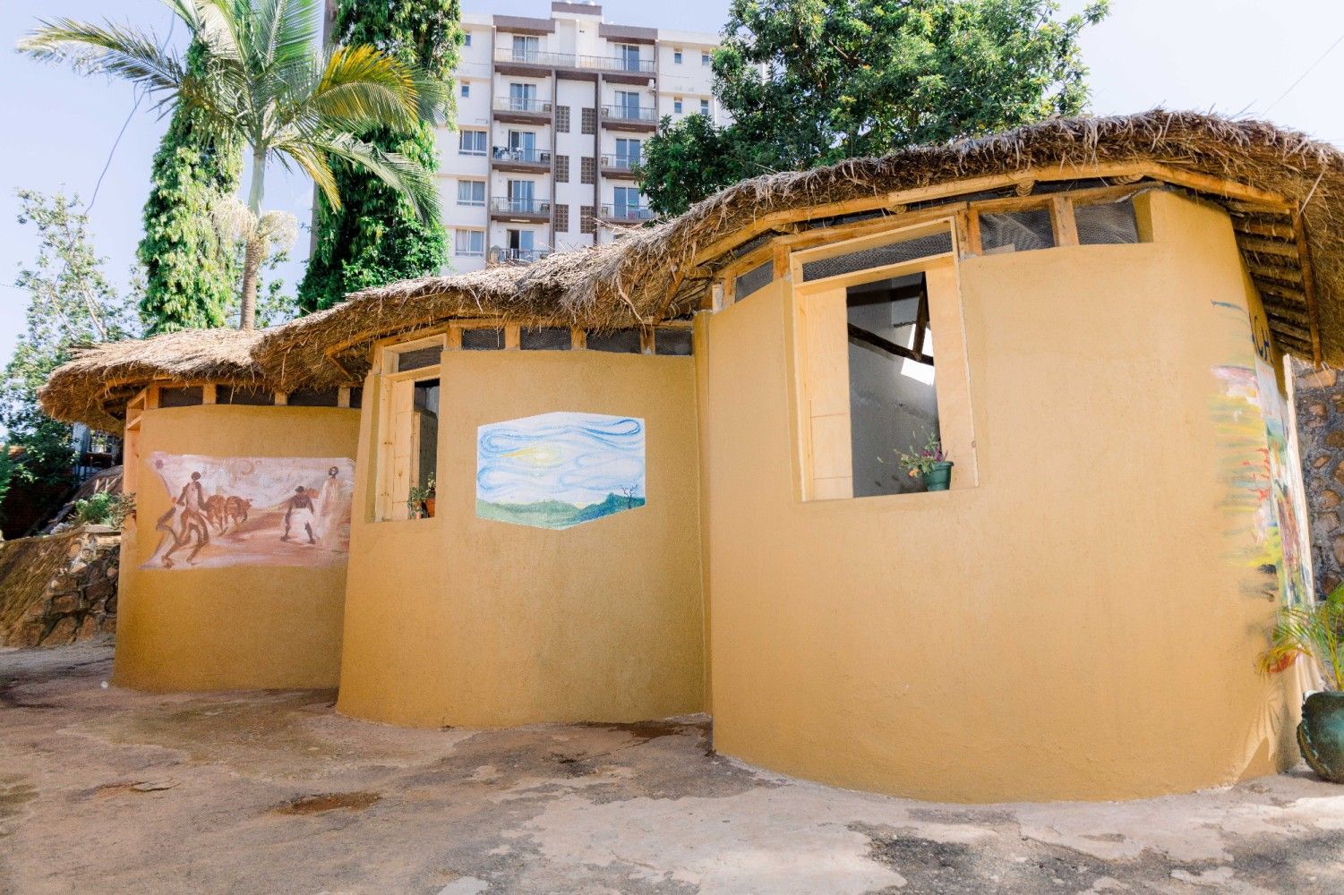Curved yellow hut with thatched roof and small windows in a sunny outdoor courtyard.