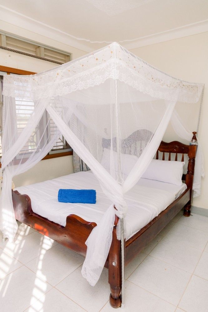 White canopy bed with sheer mosquito net in a bright bedroom, with a blue towel on the bed
