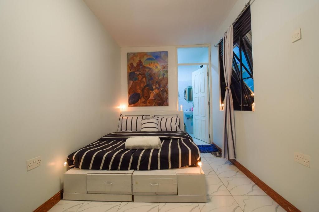 Small bedroom with a bed, striped bedding, wall art, and a window beside a mirrored wardrobe.