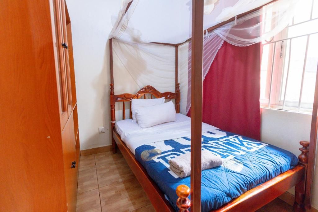 Bedroom with wooden four-poster bed, blue blanket, white pillows, and pink curtains by a window