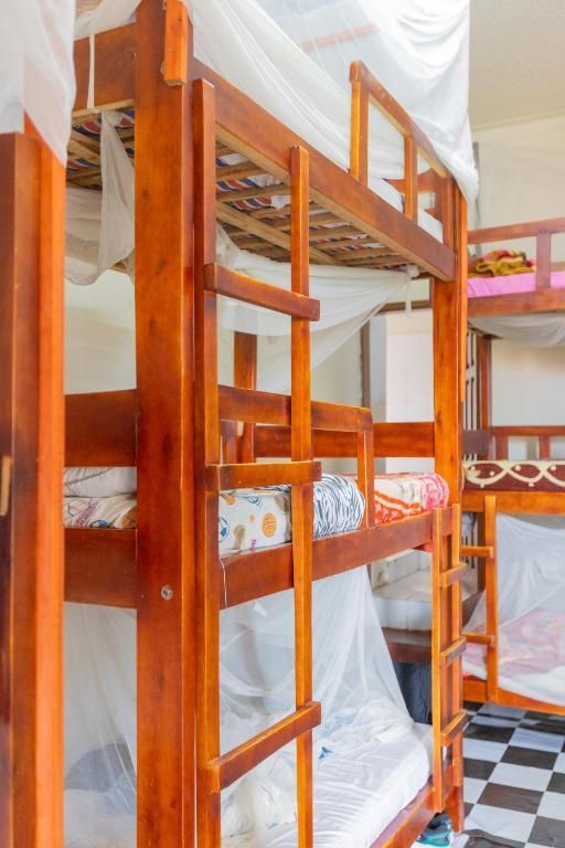 Wooden bunk beds in a bright hostel dorm with white curtains and checkered floor.