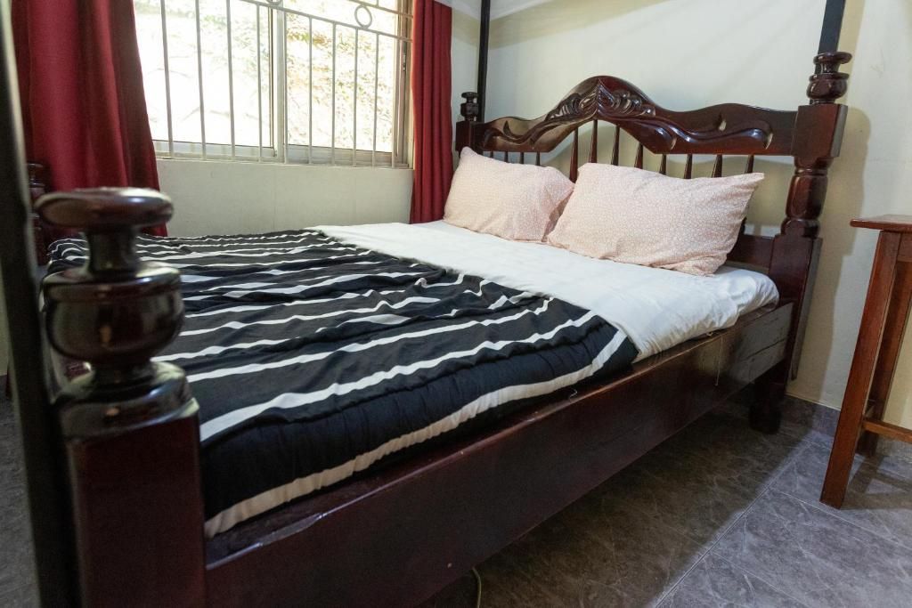 Bedroom with wooden bed, black patterned blanket, white pillows, and red curtains by a window