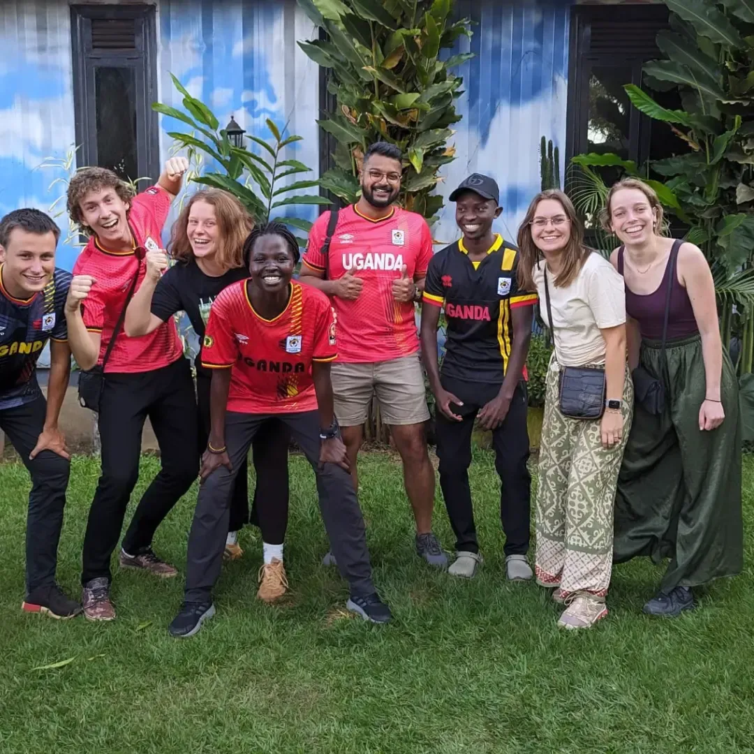 Group of people posing outdoors on grass in front of a building, smiling and wearing colorful shirts.