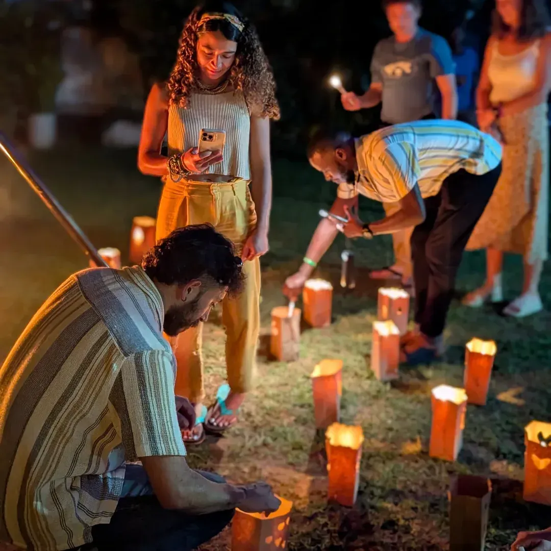 People placing candles outdoors at night in a small memorial circle