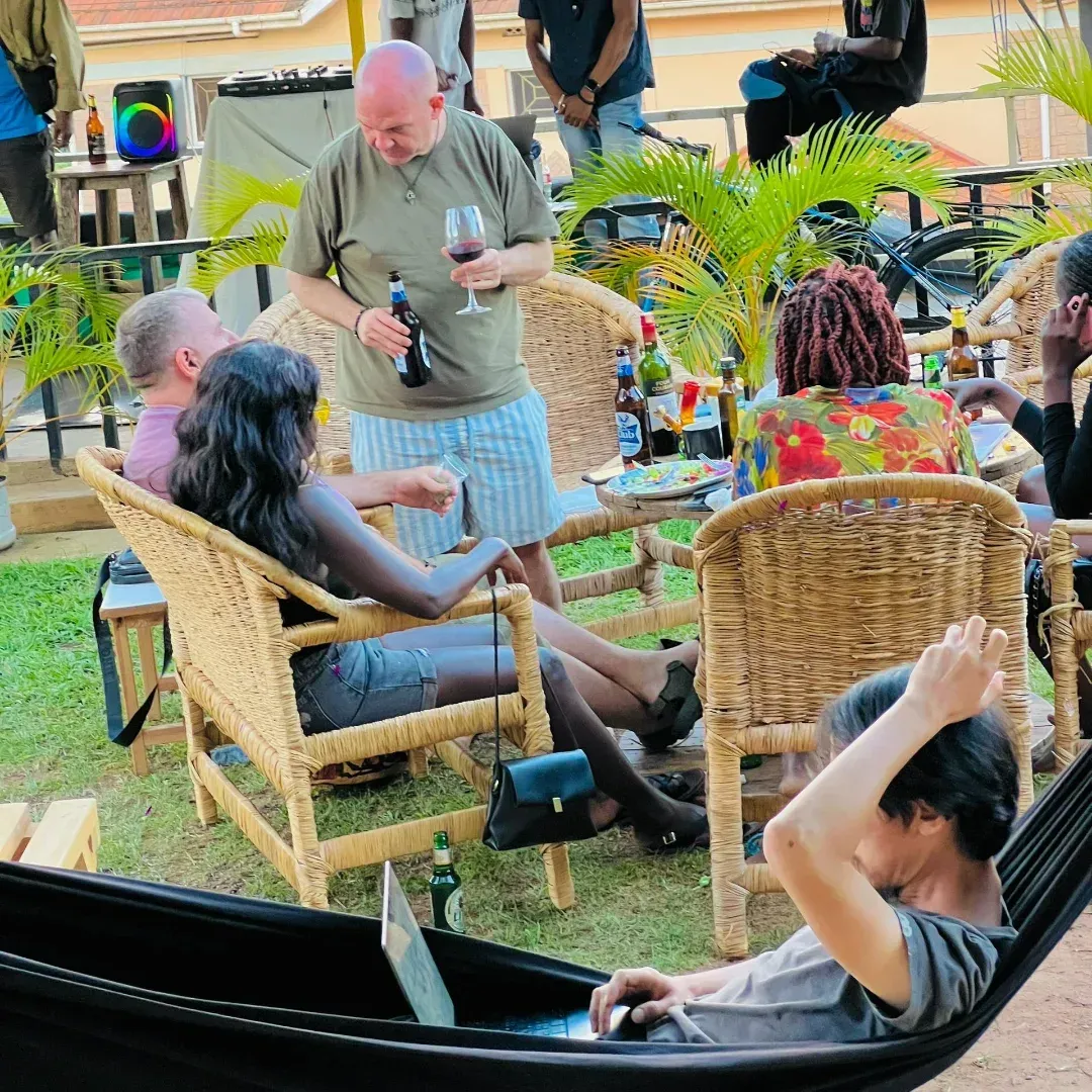 People seated in wicker chairs at an outdoor gathering, with a man pouring a drink amid tropical plants.