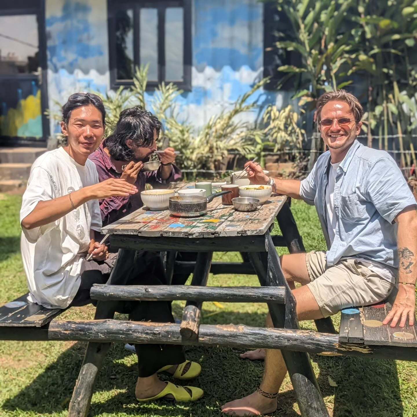 Two people and a dog sitting at a picnic table outdoors in bright sun