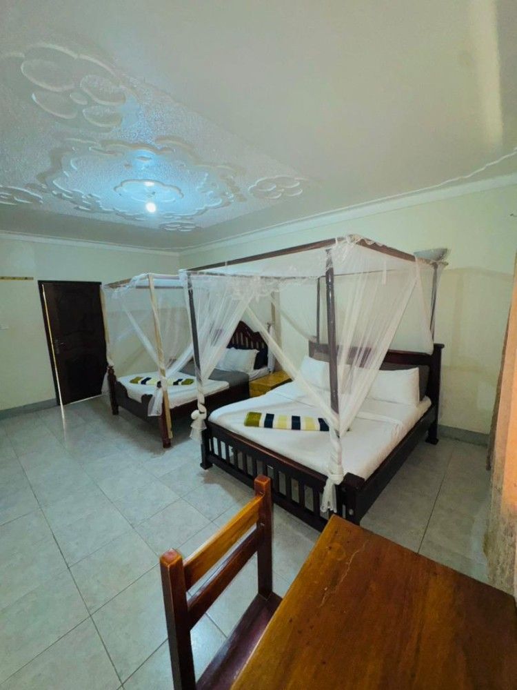 Bedroom with two canopy beds, sheer white curtains, dark wood furniture, and tiled floor