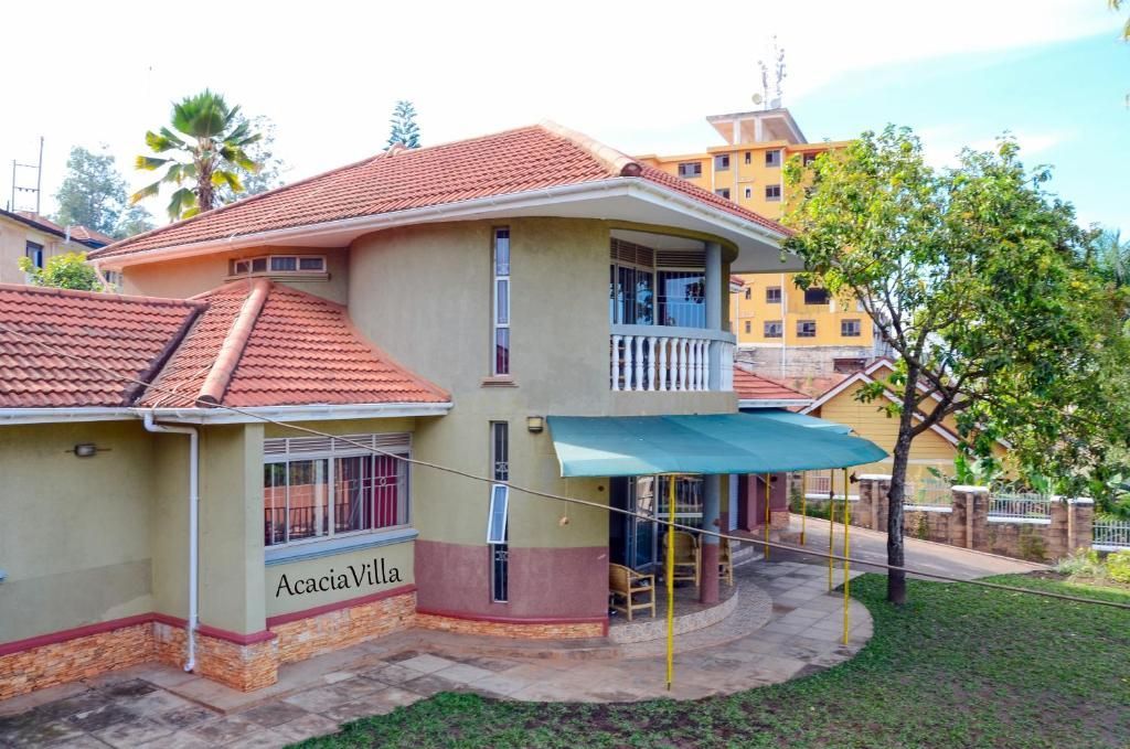 Large beige house with red tile roof, blue awning, and balcony amid trees and lawn