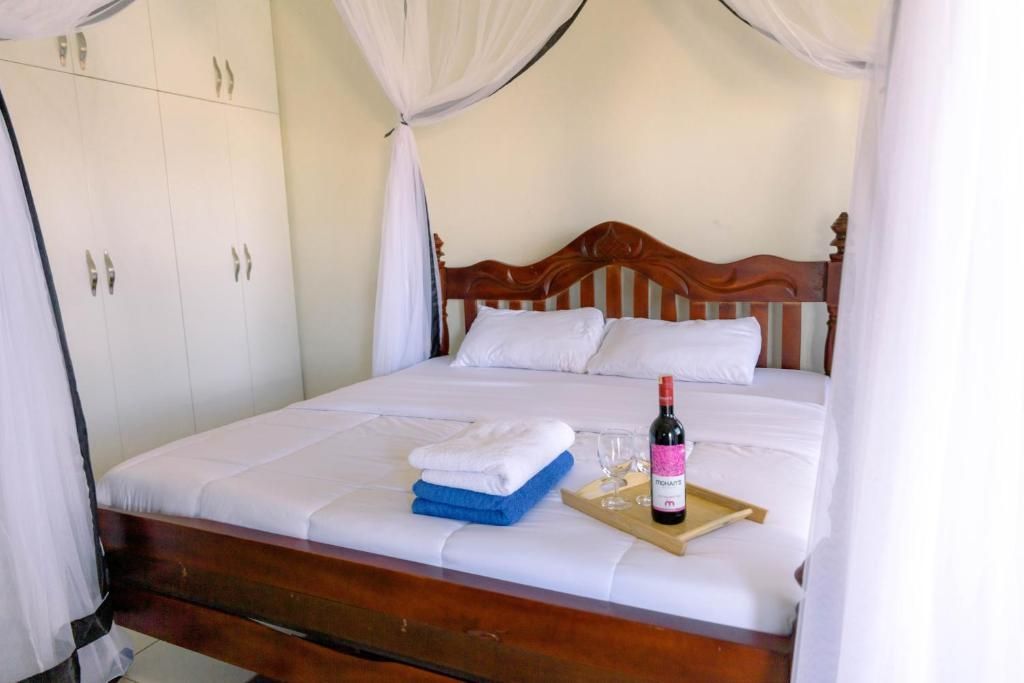 Canopy bed with white sheets, folded towels, and a bottle on the bed in a bright room