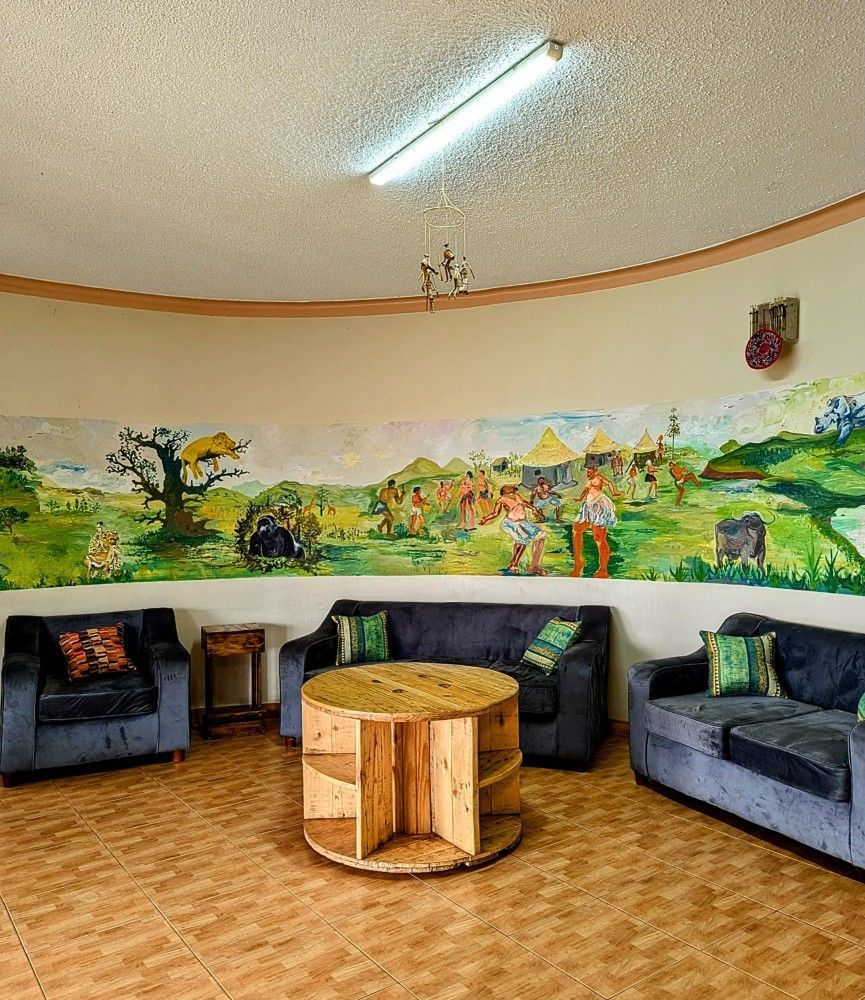 Cozy lounge with gray armchairs, a round wooden table, mural wall art, and a ceiling light.