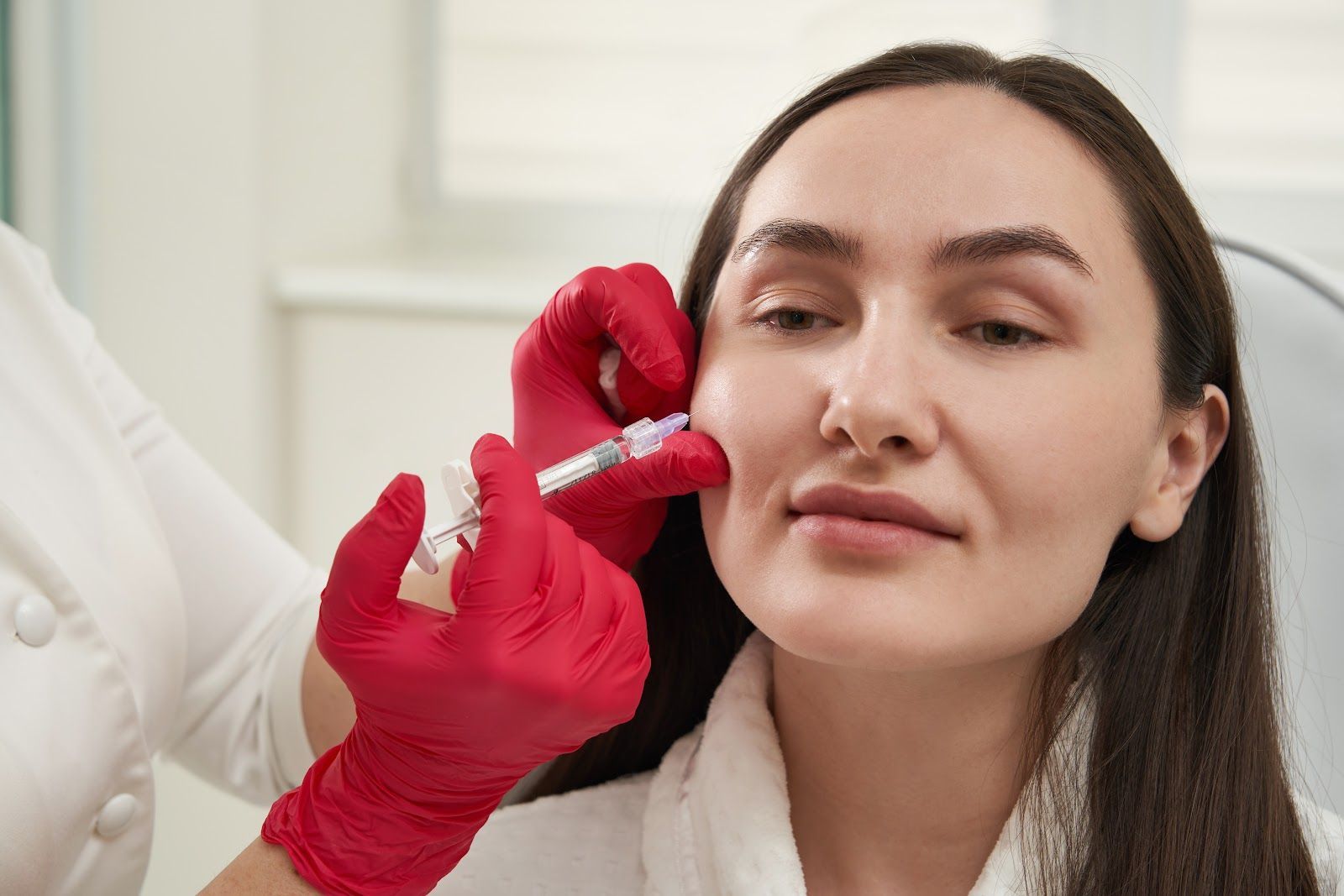 Gloved hands inject filler into a woman’s cheek in a clinical setting