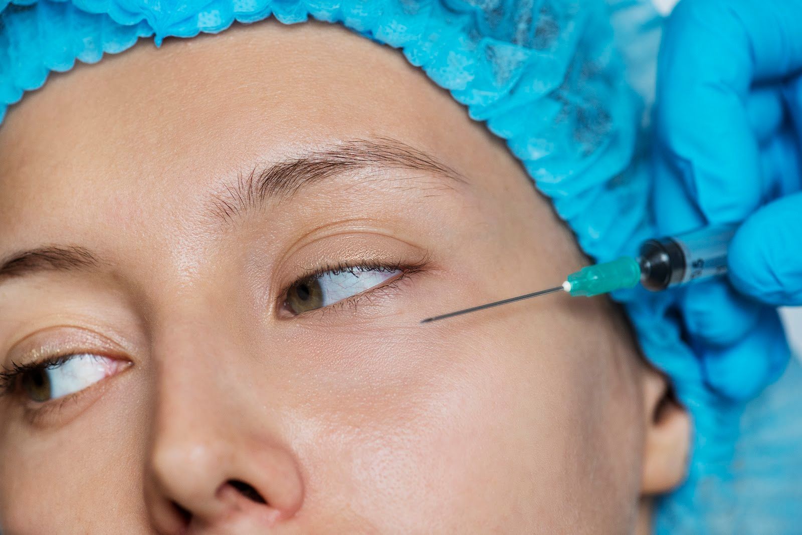Close-up of an eye area as a gloved hand applies a fine cosmetic injection near the temple