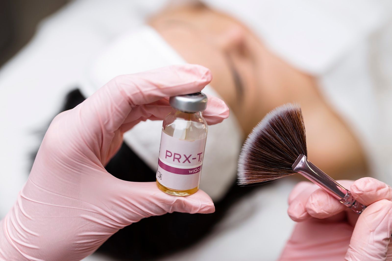 Gloved hands holding a PRX-T vial and a facial brush during a skincare treatment