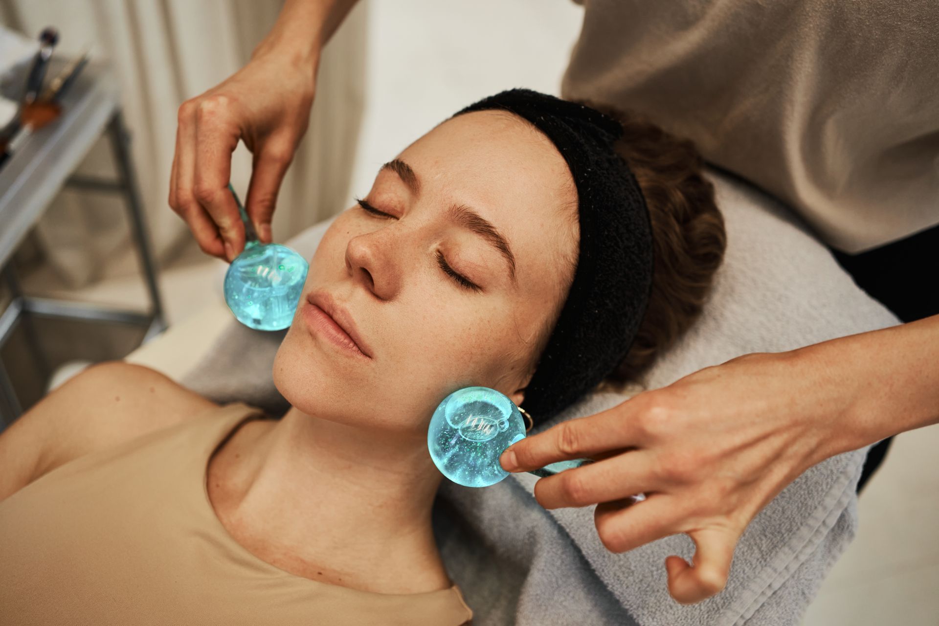 Spa therapist holding blue facial tools near a relaxed client’s face during a treatment