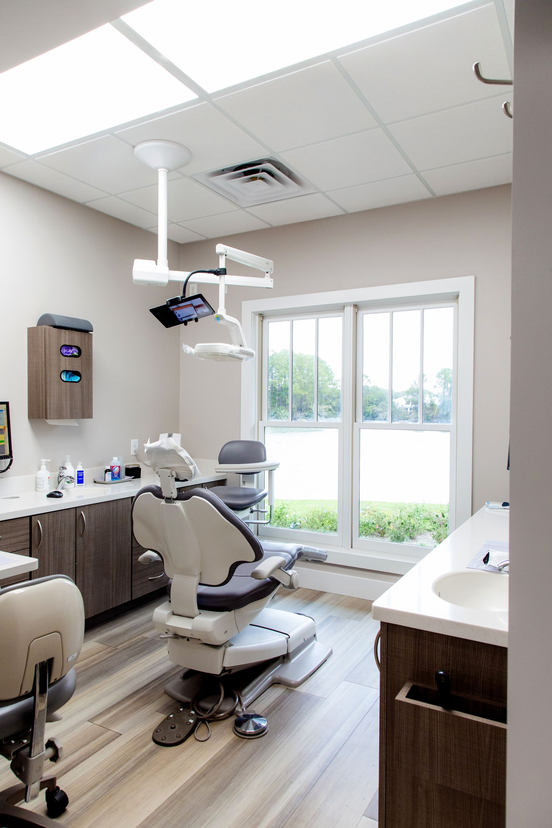 Modern dental exam room with chair, overhead lights, cabinets, and large window.