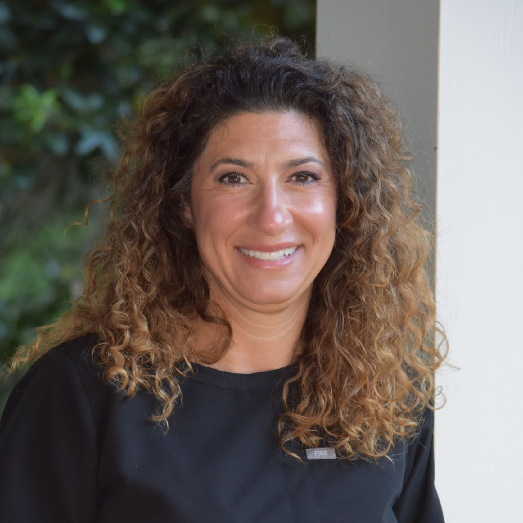 Smiling woman with curly dark hair against a light background