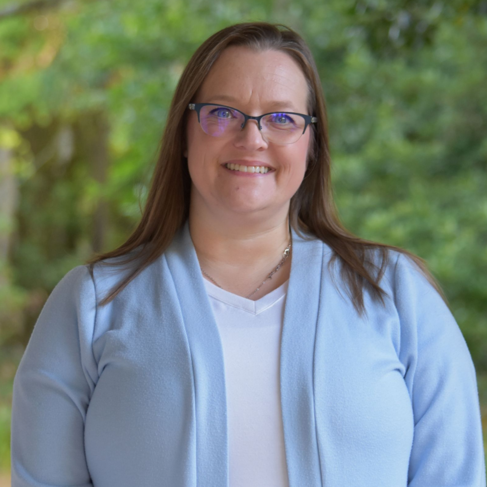 Smiling woman in glasses standing with folded arms beside a yellow wall outdoors