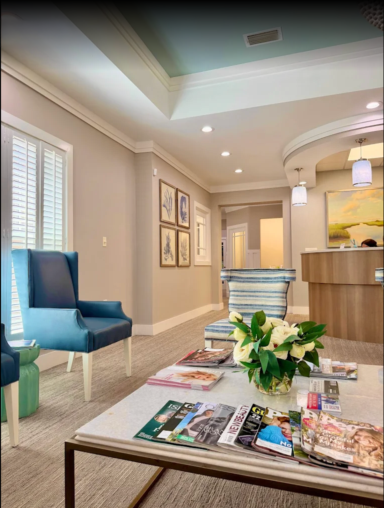 Bright modern office lobby with blue chairs, coffee table, flowers, magazines, and reception desk