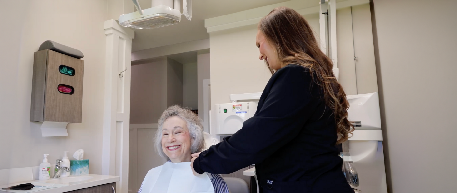Dentist smiling while examining a patient reclining in a dental chair