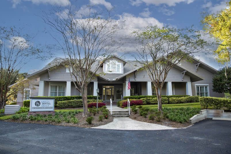 A white clubhouse with a front porch, green shrubs, and a curved walkway under a blue sky.