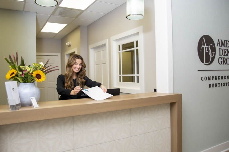 Reception desk with smiling staff member in a bright office lobby, holding papers and answering the phone