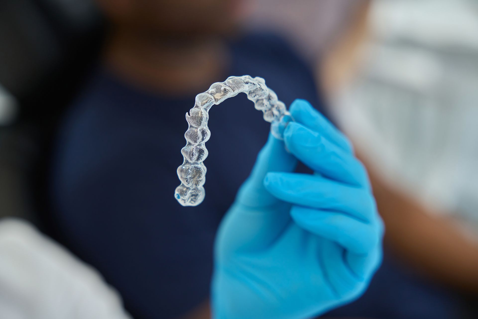 Smiling woman holding clear dental aligners in a bathroom mirror