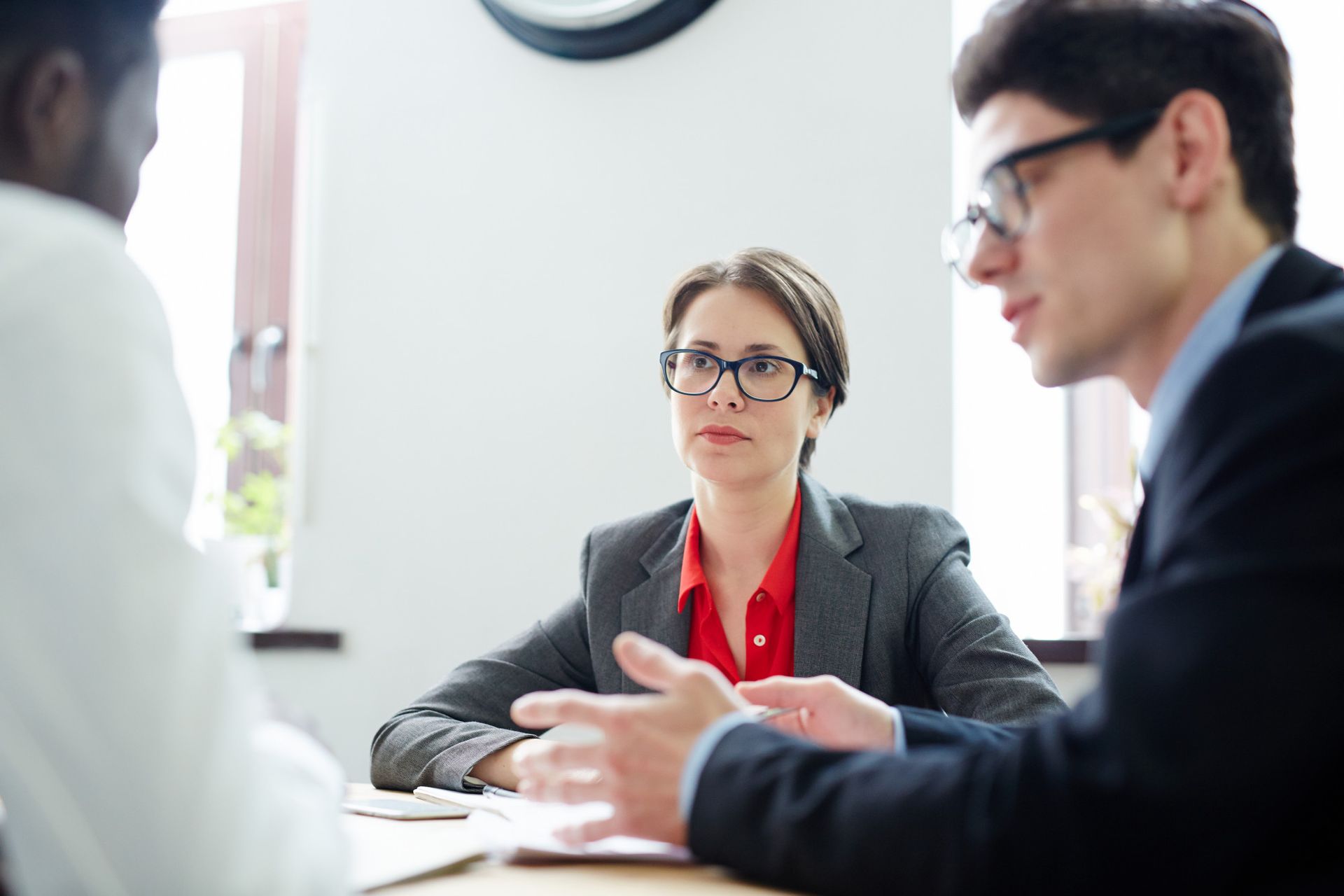 Three businesspeople in a meeting, with a woman in a gray blazer listening attentively.