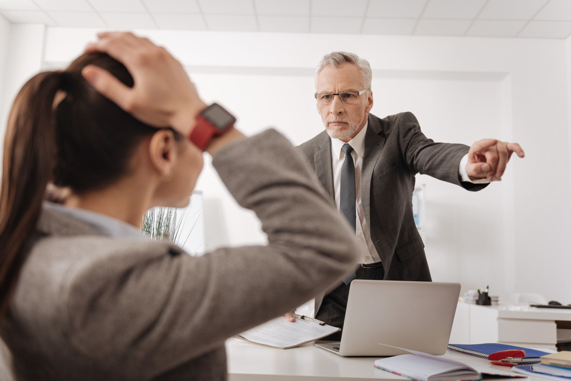 A man in a suit and tie is pointing at a woman in an office.