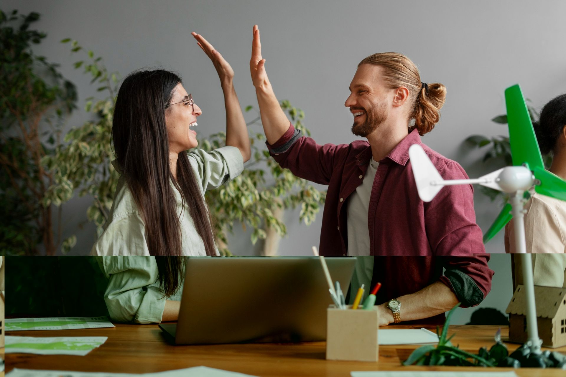 A man and a woman are giving each other a high five in front of a wind turbine.