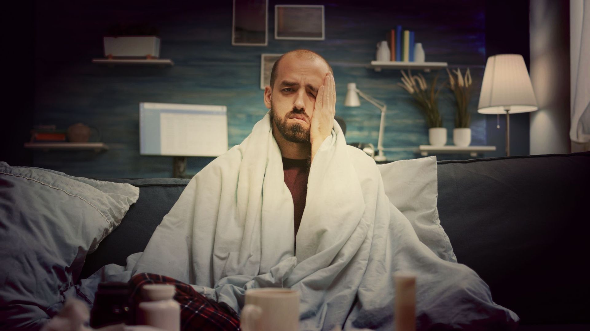 A man is sitting on a couch wrapped in a blanket.