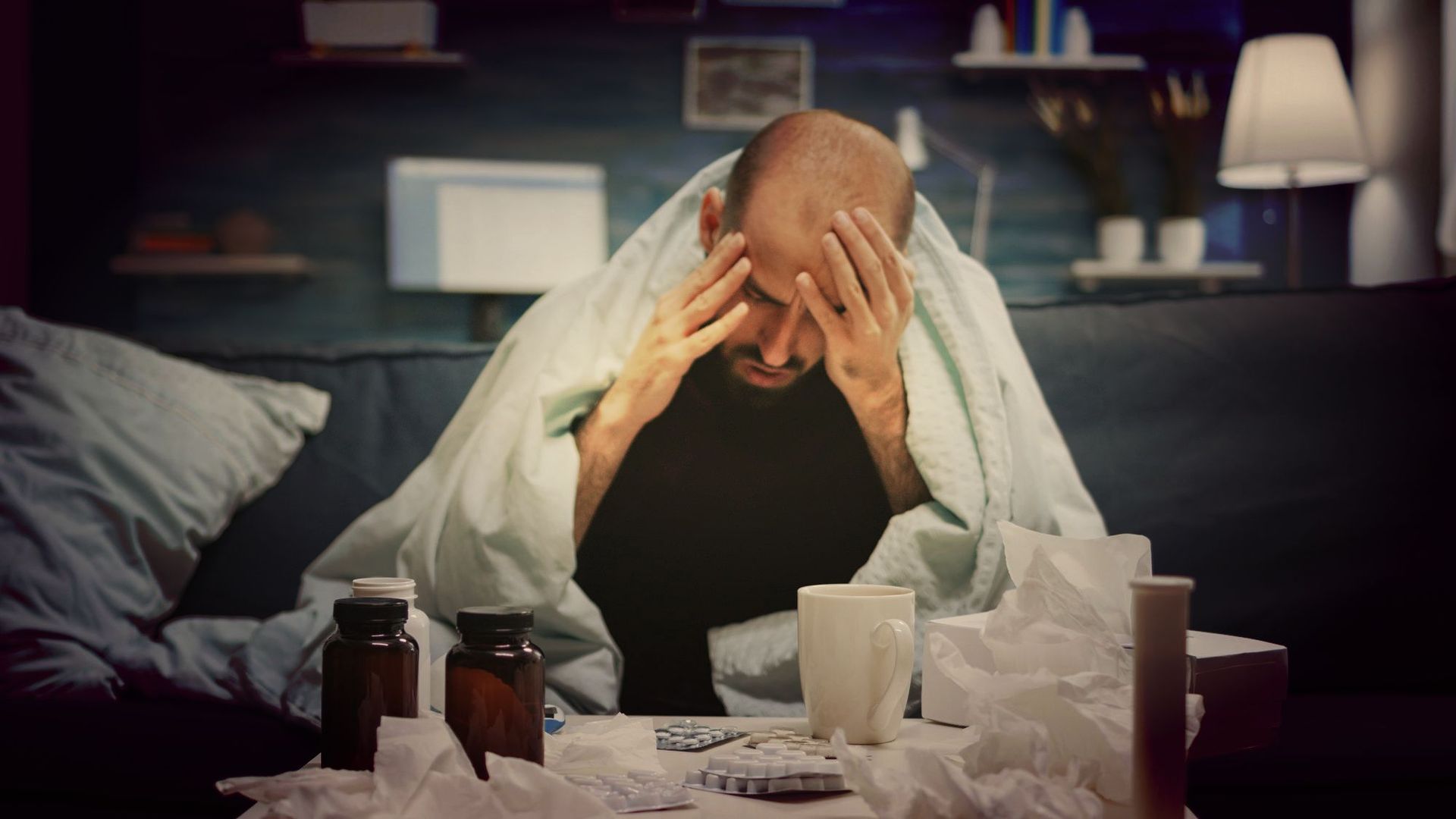 A man is sitting on a couch with his head in his hands.