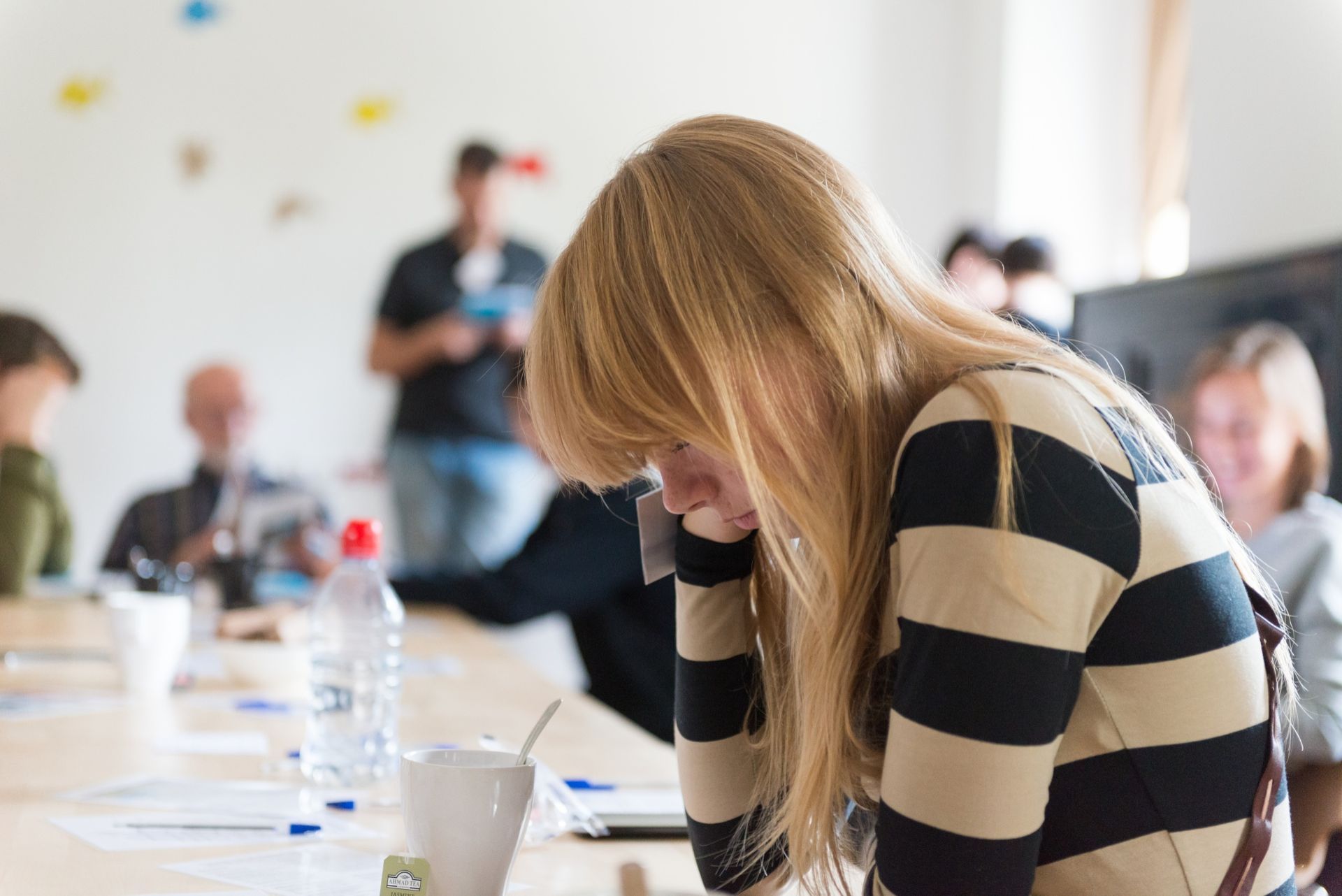 Person in striped sweater sitting at a conference table, leaning on their hand in a meeting room
