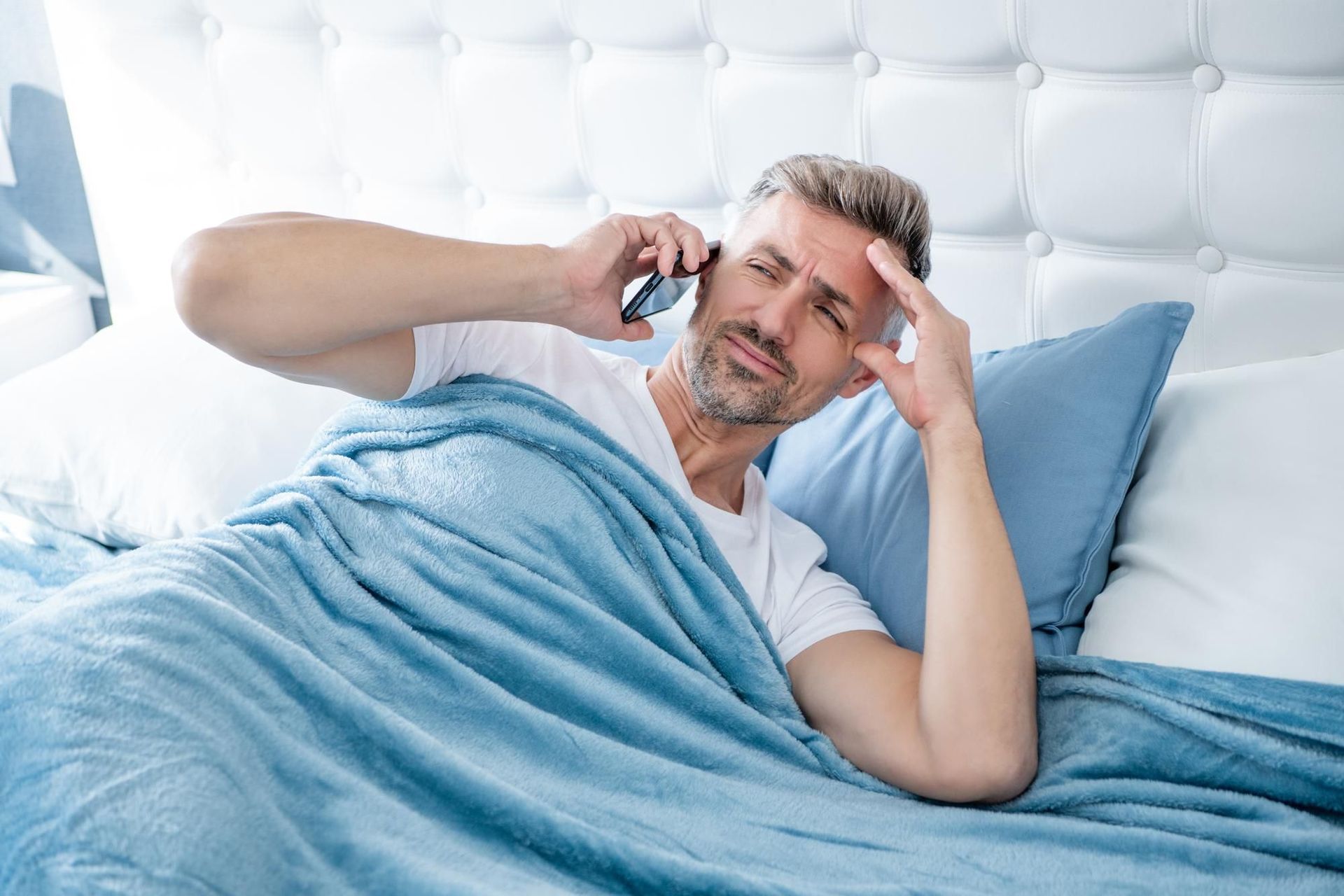 A man is laying in bed talking on a cell phone.