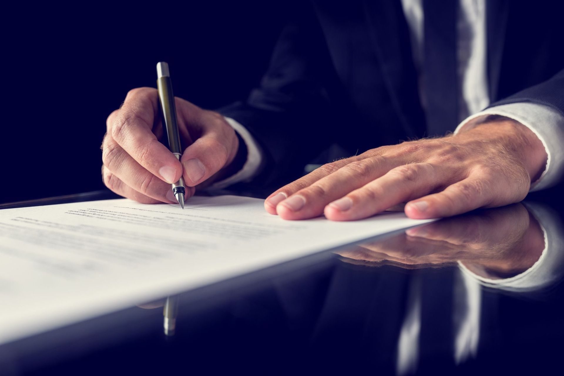 A man in a suit is writing on a piece of paper with a pen.