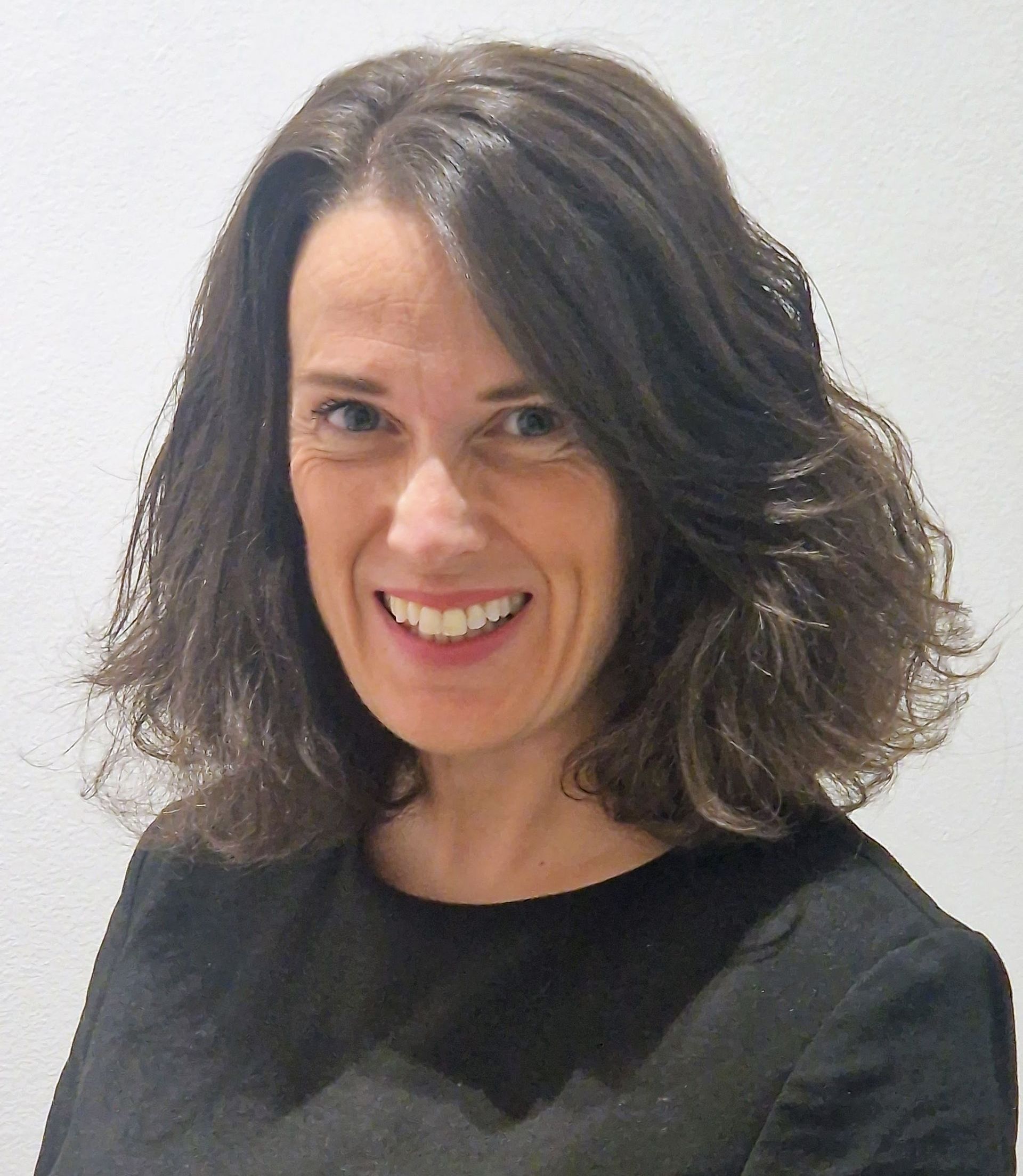 A woman with long brown hair is wearing a black sweater and smiling for the camera.