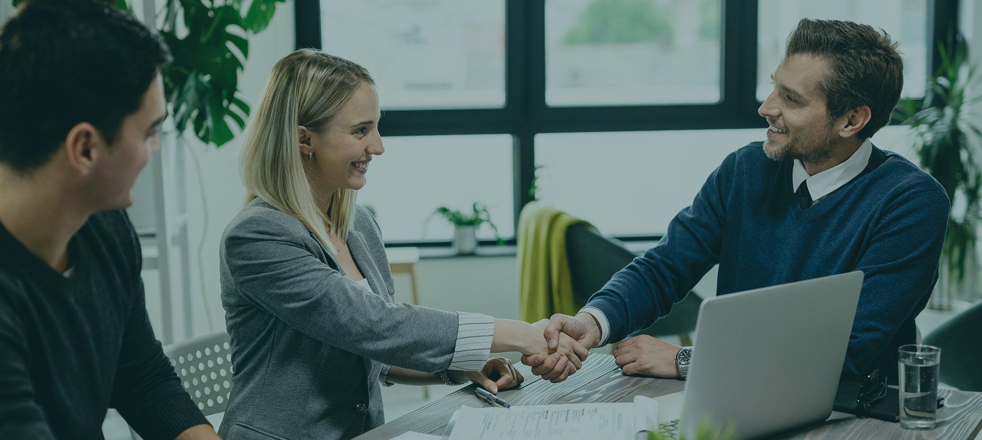 A man and a woman are shaking hands while sitting at a table with a laptop.